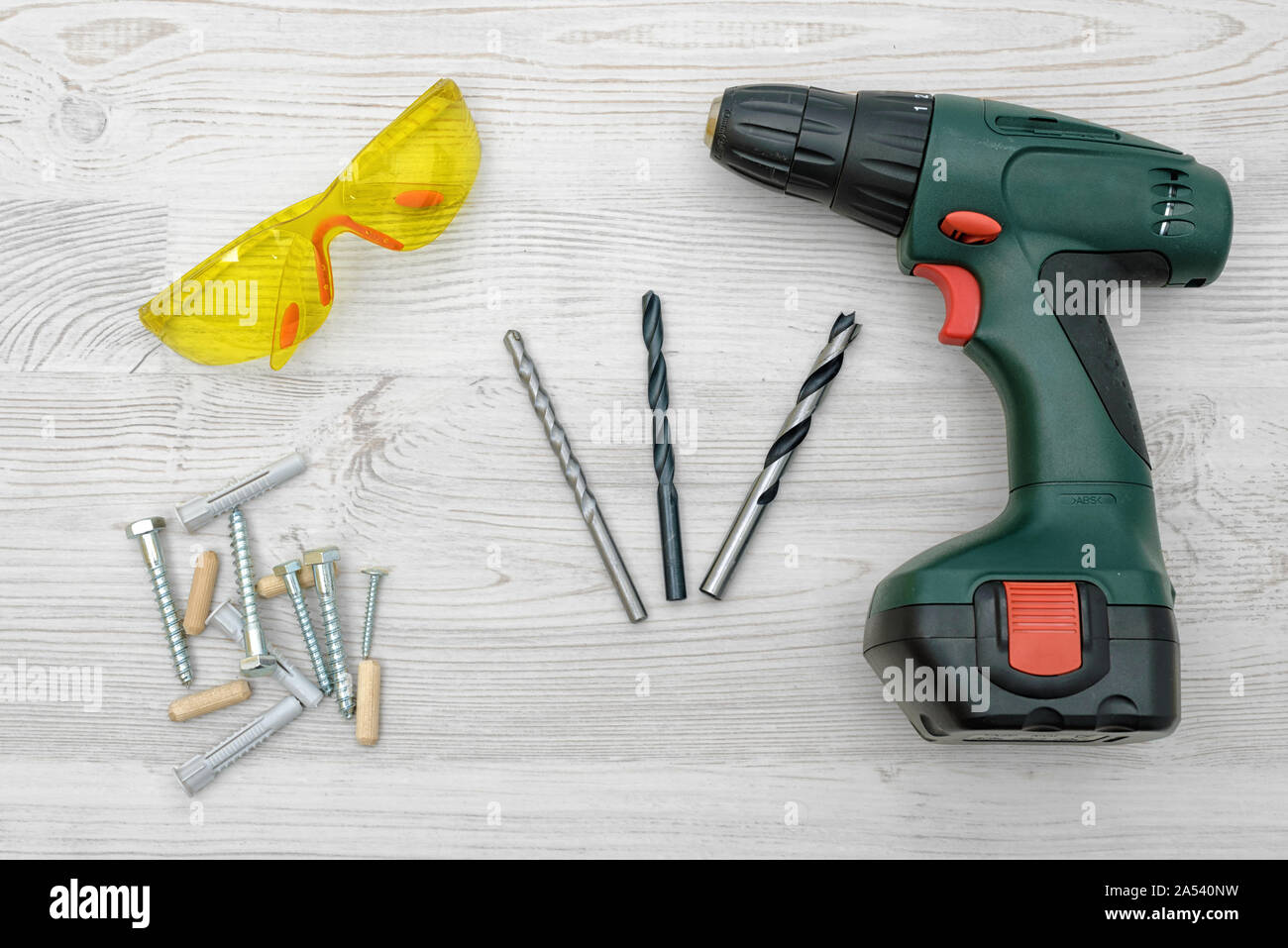 https://c8.alamy.com/comp/2A540NW/a-cordless-drill-set-on-a-wooden-table-background-with-a-set-of-bits-in-the-box-and-yellow-protective-glasses-around-2A540NW.jpg