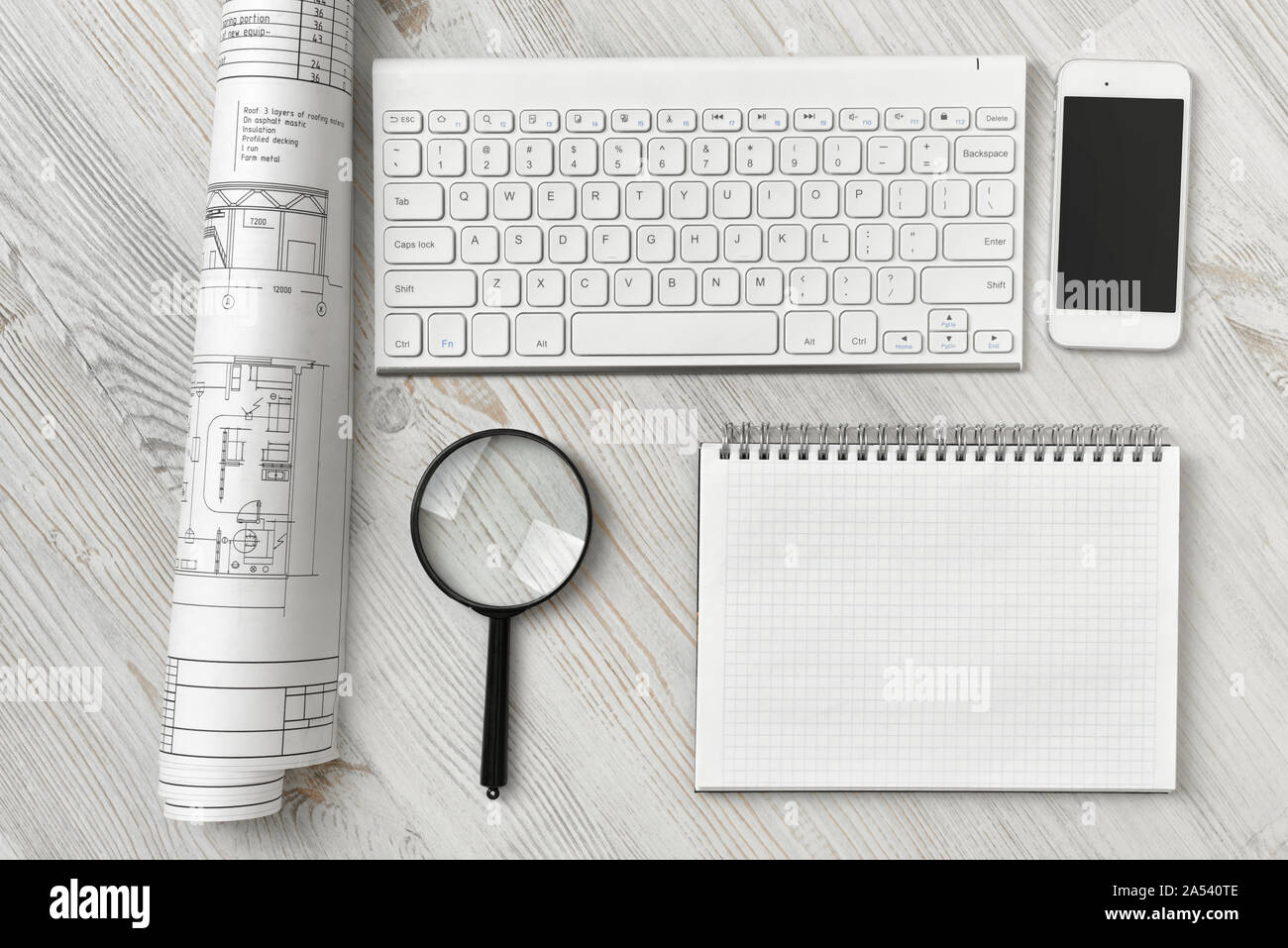 Office workspace with architectural drawing, keyboard, smarthphone, clean book and magnifier on wooden surface in top view Stock Photo
