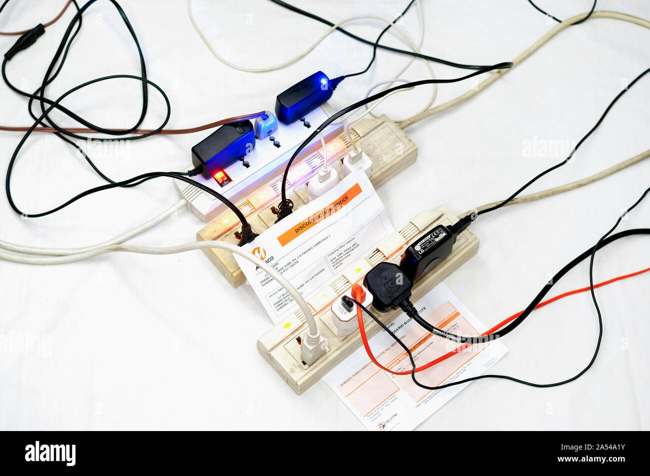 Multiple overloaded power boards extension socket with a MERALCO Disconnection Notice on white isolated background. Stock Photo