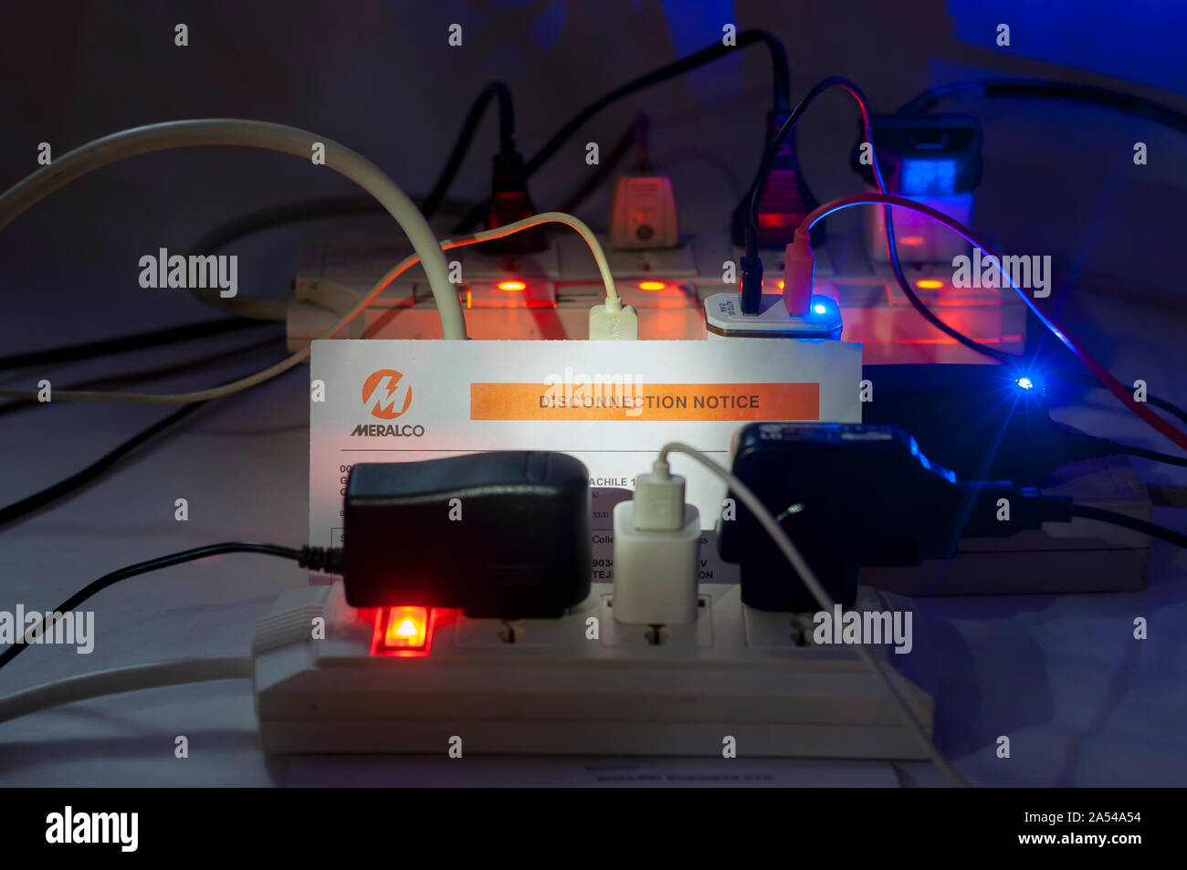 Dramatic night shot of multiple overloaded power boards extension socket with a MERALCO Disconnection Notice. Stock Photo