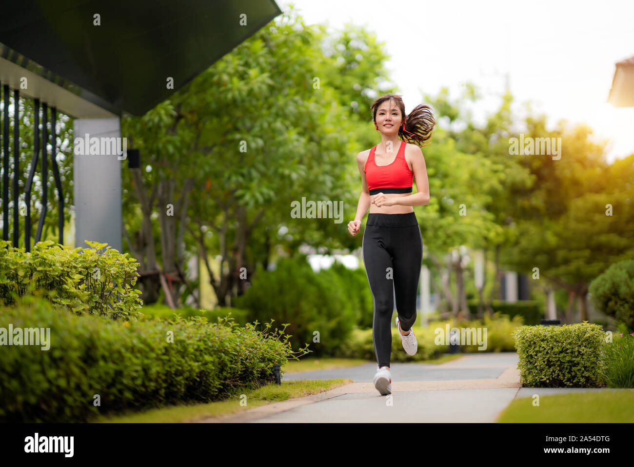 Asian beautiful woman exercising running alone in public park in village, happy and smile in morning during sunlight. Sport fitness model Asian ethnic Stock Photo