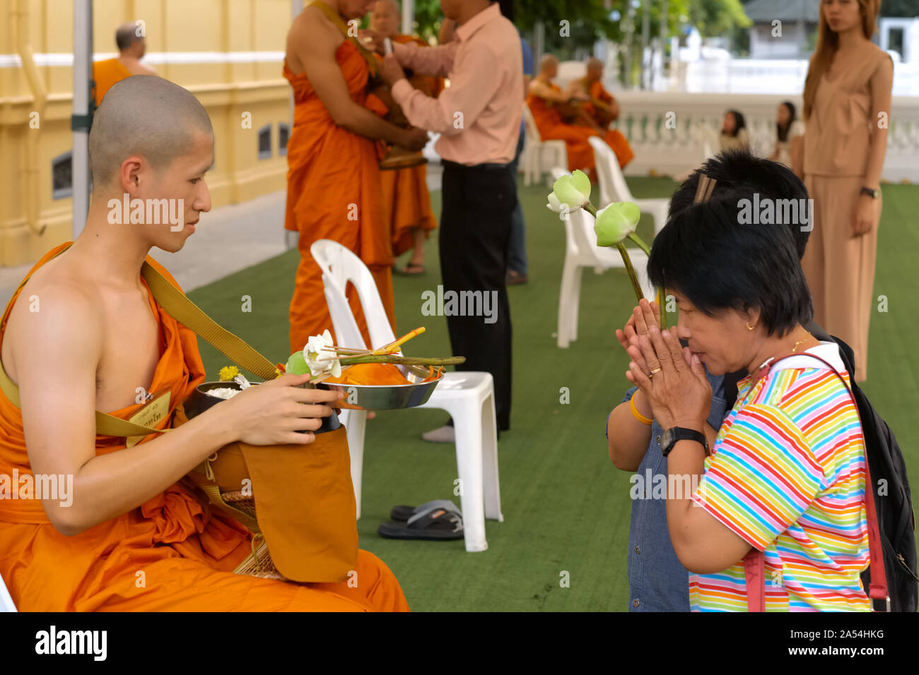 A female relative of a freshly ordained Buddhist monk honors him with a customary Thai 'wai' (polite greeting); Wat Boworniwet, Bangkok, Thailand Stock Photo