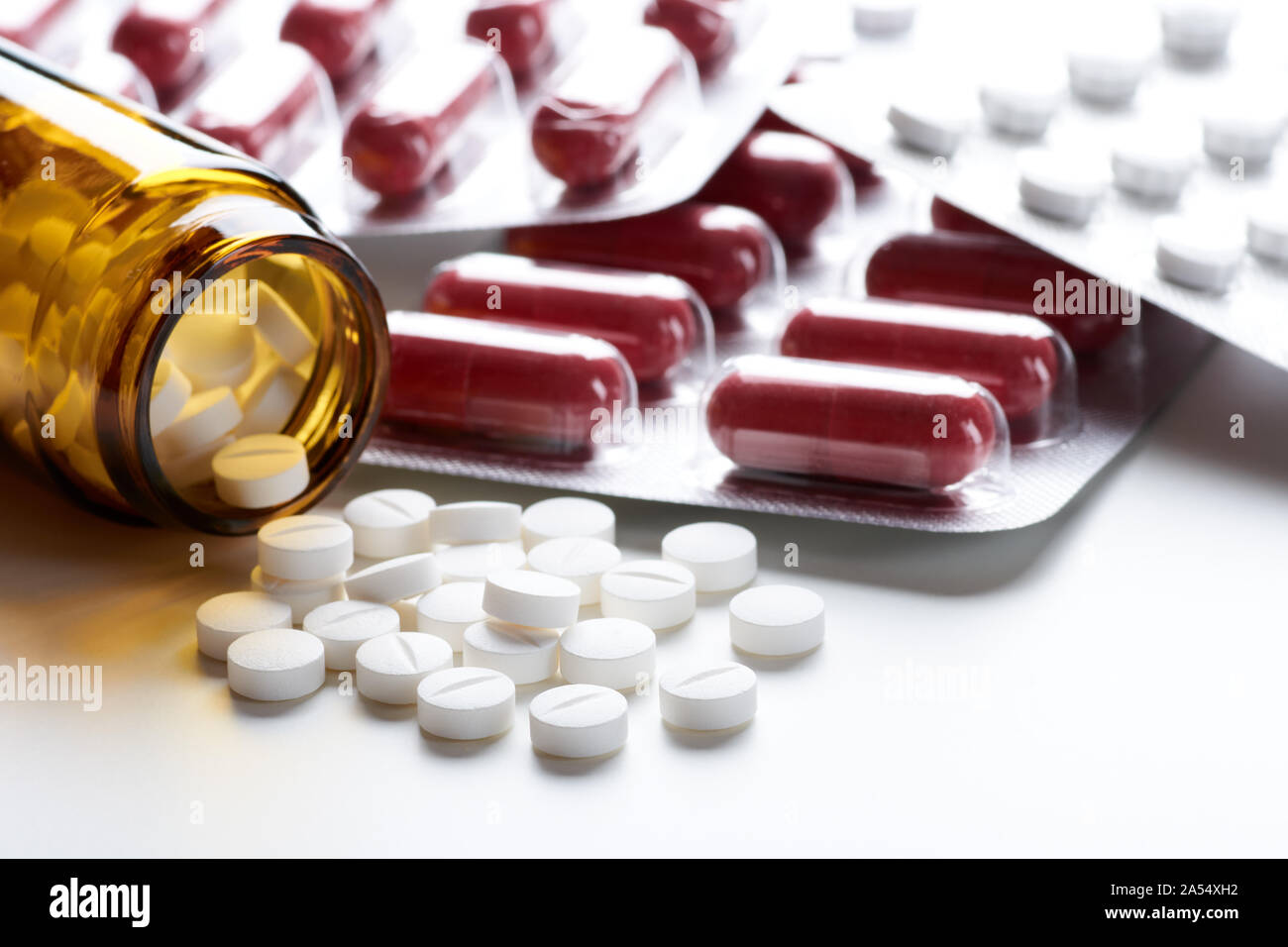 Pile of tablets and pills in bottle, glass and blister pack on white table top with space for text Stock Photo