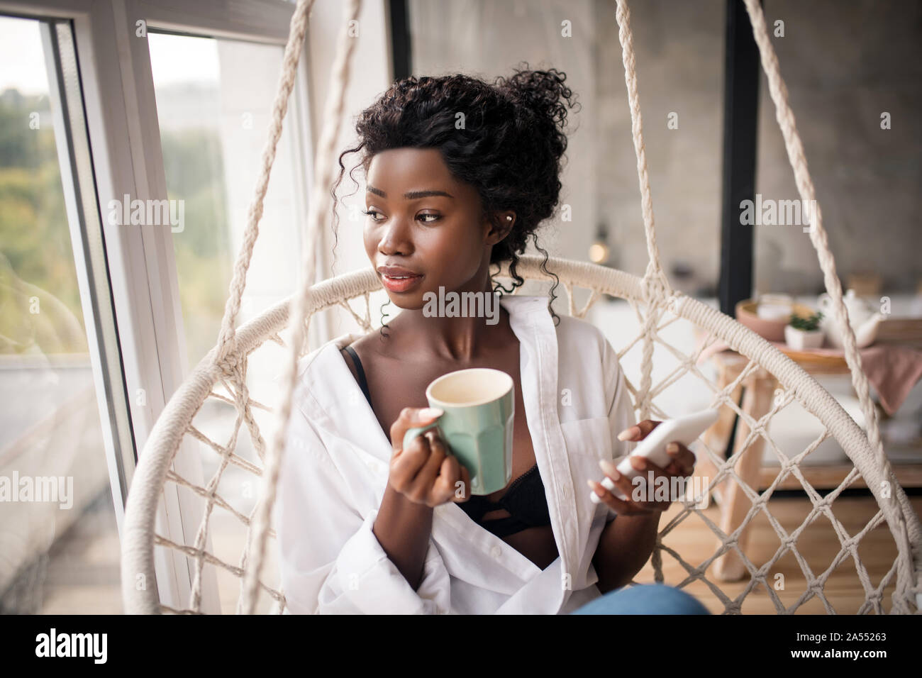 Curly woman looking into window while enjoying coffee Stock Photo