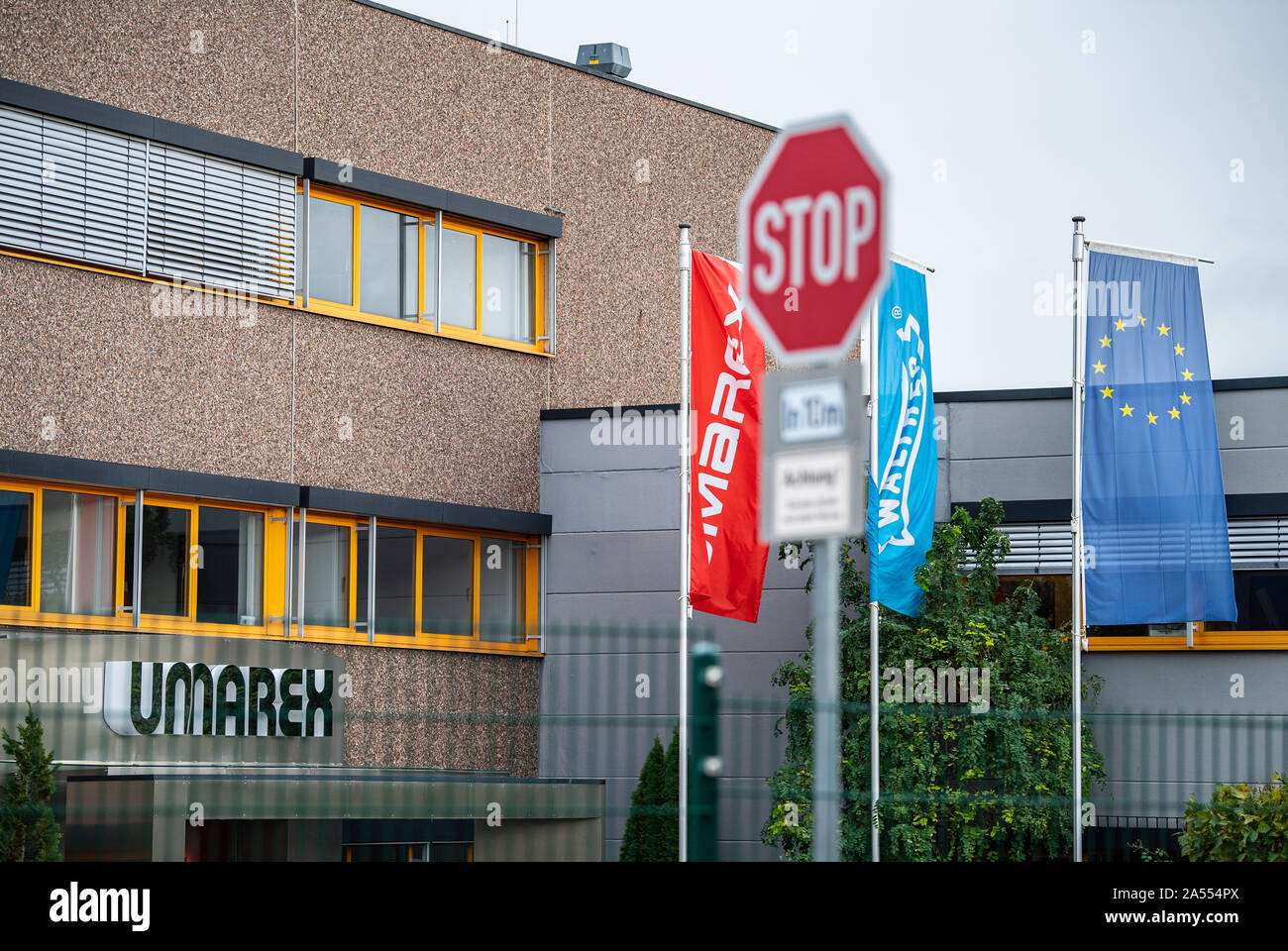 17 October 2019, North Rhine-Westphalia, Arnsberg: The company logo hangs on the outer facade of the weapons manufacturer Umarex, in front of which a flag of the weapons brand Walther is flying. Because for years he is said to have smuggled pistol parts from a weapons manufacturer's factory, assembled and sold them, a 47-year-old man is now on trial in Arnsberg, Sauerland. Since 2015, the long-time employee of the Arnsberg-based sporting weapons manufacturer Umarex has been reported to have repeatedly stolen design drawings and weapon parts from his former employer and assembled them into func Stock Photo