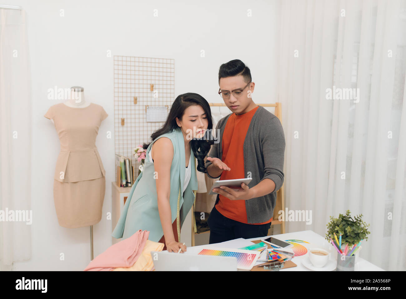 Two young woman and man fashion designers working and using tablet together at the studio Stock Photo