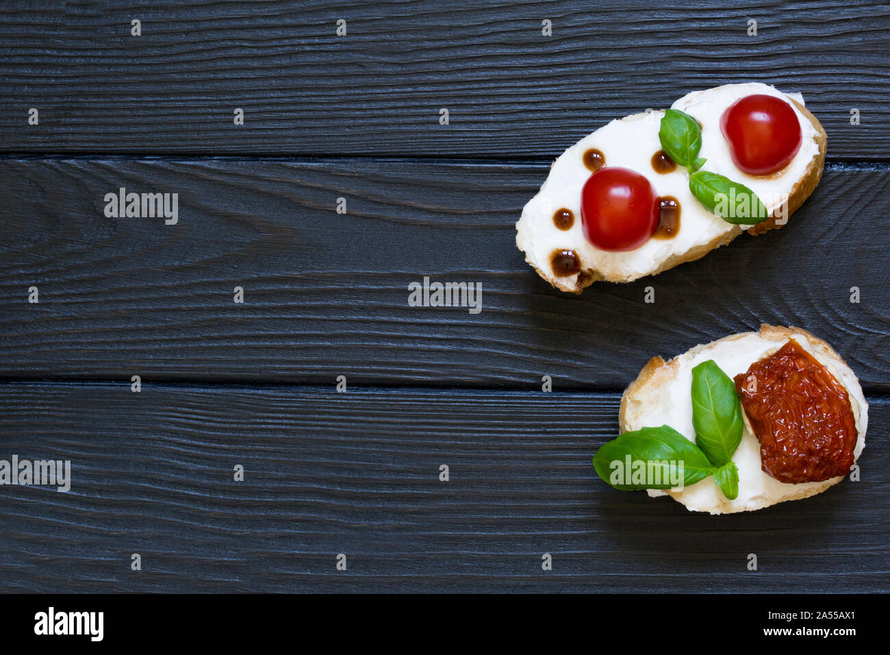 Bruschettas with tomatos, goat white cheese, dry tomato and basil on the black rustic wooden  background. Italian cuisine, top view. Copy space. Stock Photo