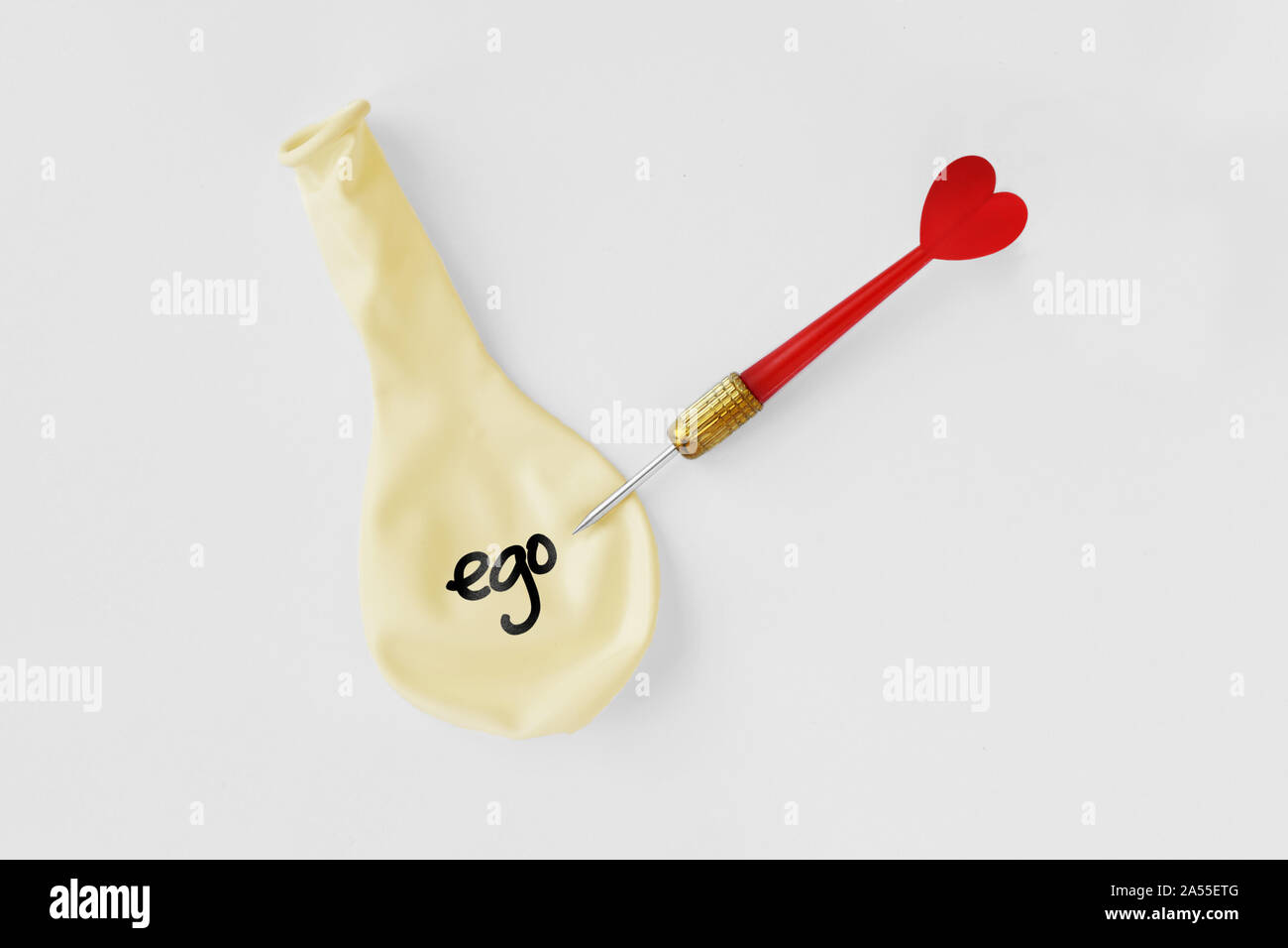 Deflated balloon with the word ego on it and arrow dart with heart on white background - Ego and love concept Stock Photo