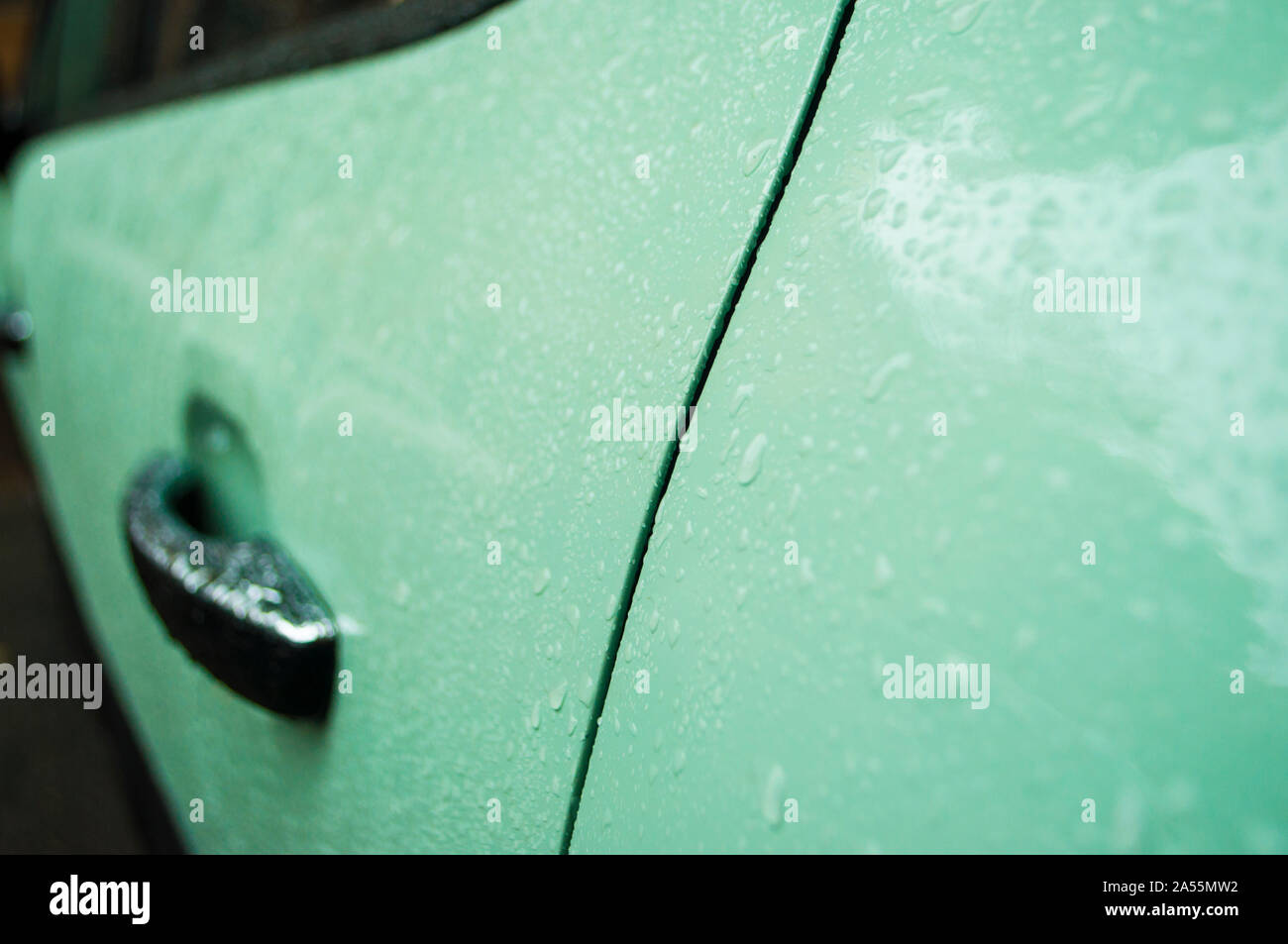 Beautiful rain drops on the car of trendy biscay green or neo mint color. Wet car body of trendy tranquil dawn color. Stock Photo