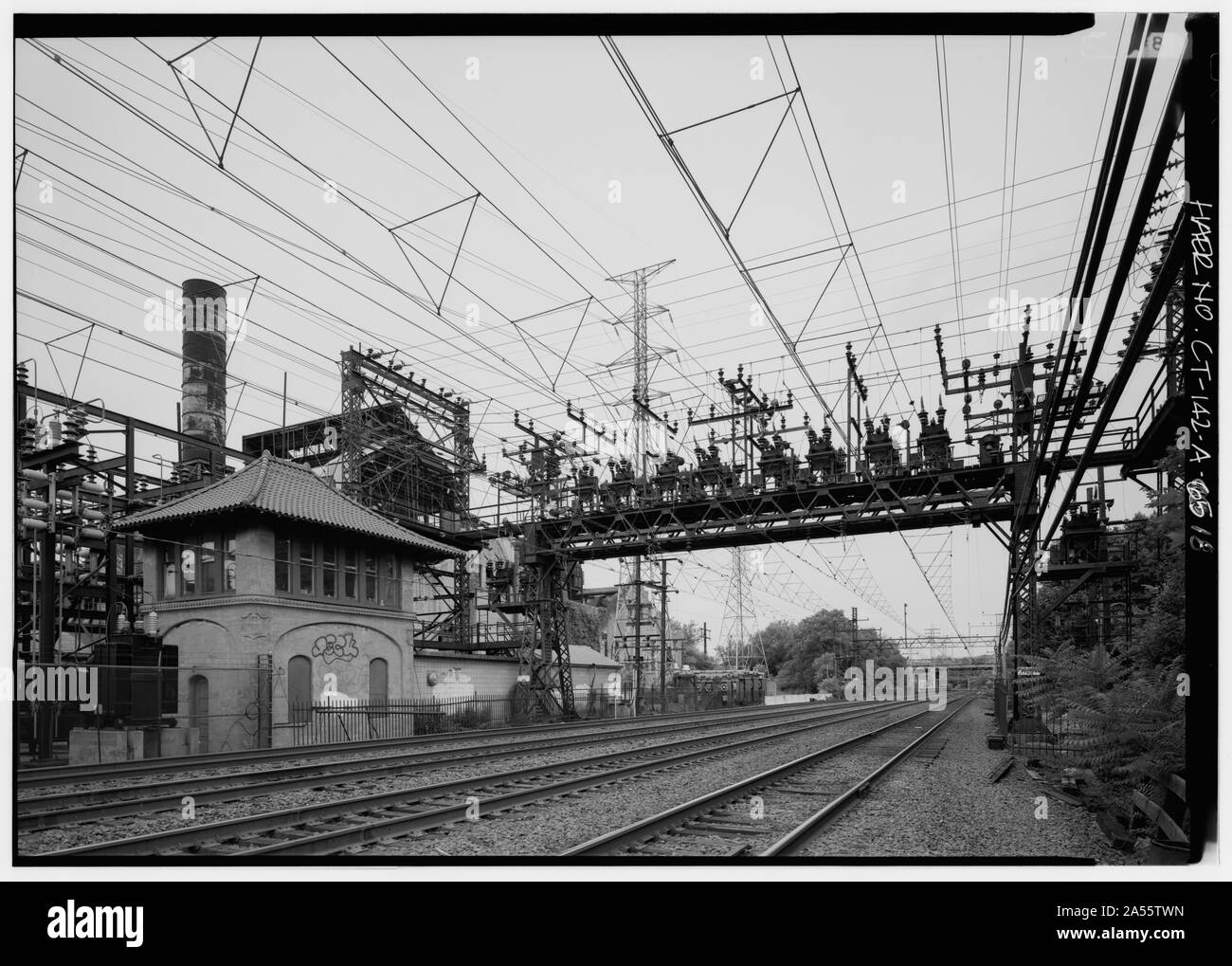 View of anchor bridge number 310 looking west along the main track located to the north of the Cos Cob power plant. The load dispatcher's tower is shown in the left foreground. At this station the dispatcher controlled power output to various parts of the system. The structure serves the same purpose in 1993 and can be operated locally or remotely from Metro-North's headquarters in Manhattan. The steel structure and stack in the background are part of the boiler 902-903 installation. - New York, New Haven and Hartford Railroad, Cos Cob Power Plant, Sound Shore Drive, Greenwich, Fairfield Count Stock Photo