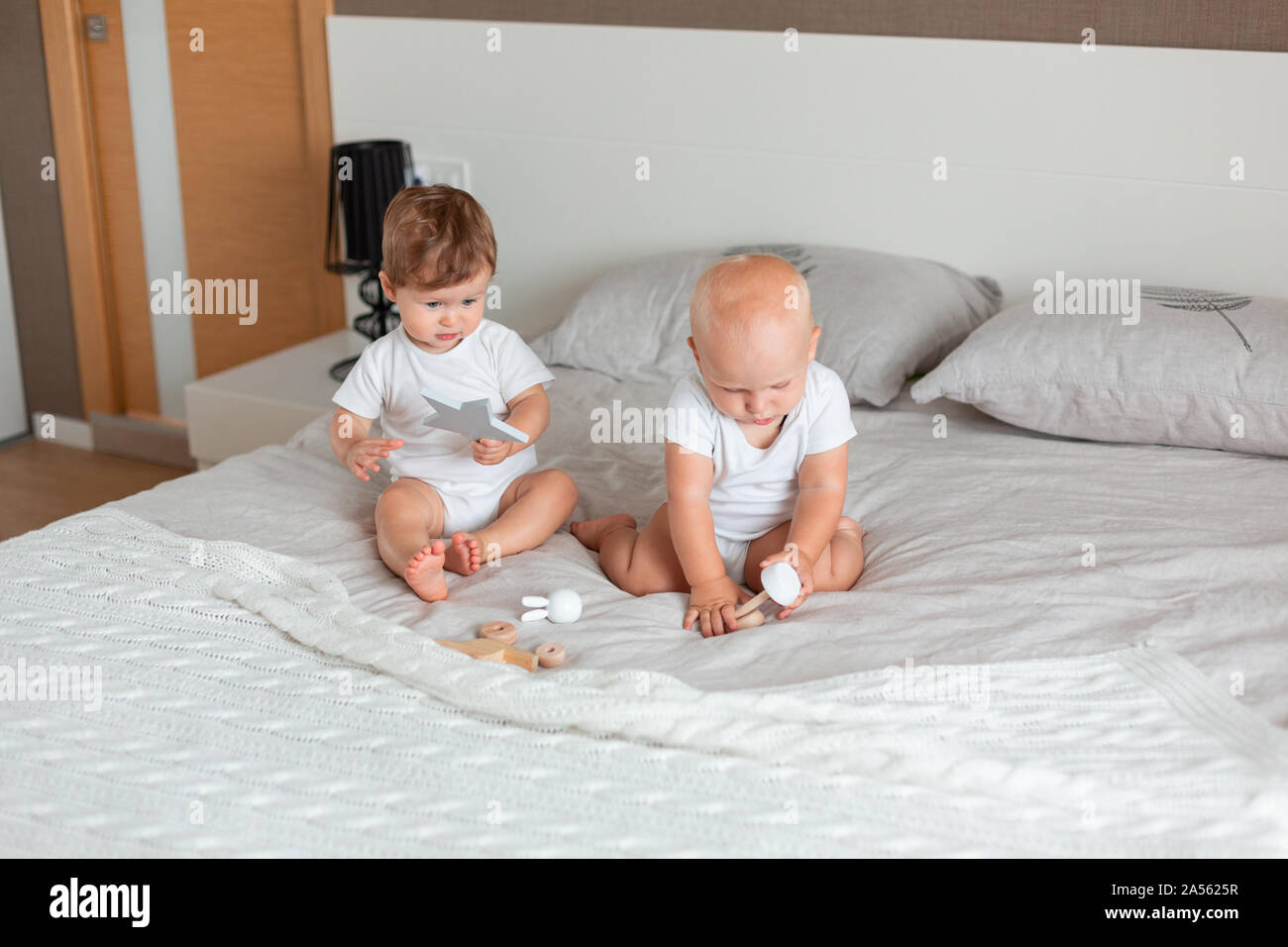 Two small happy babies sitting on a big bed in the bedroom Stock Photo ...