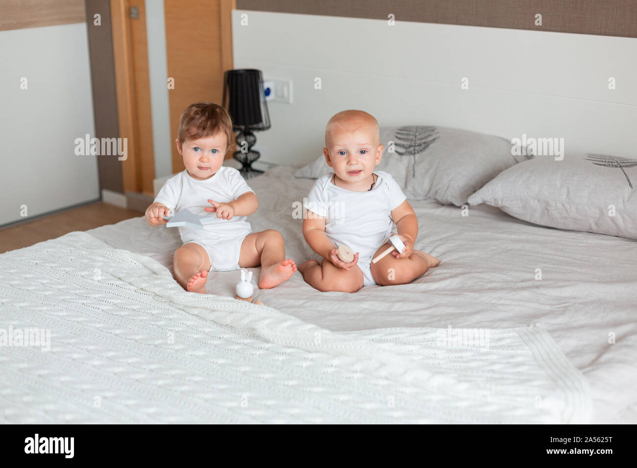 Two small happy babies sitting on a big bed in the bedroom Stock Photo ...