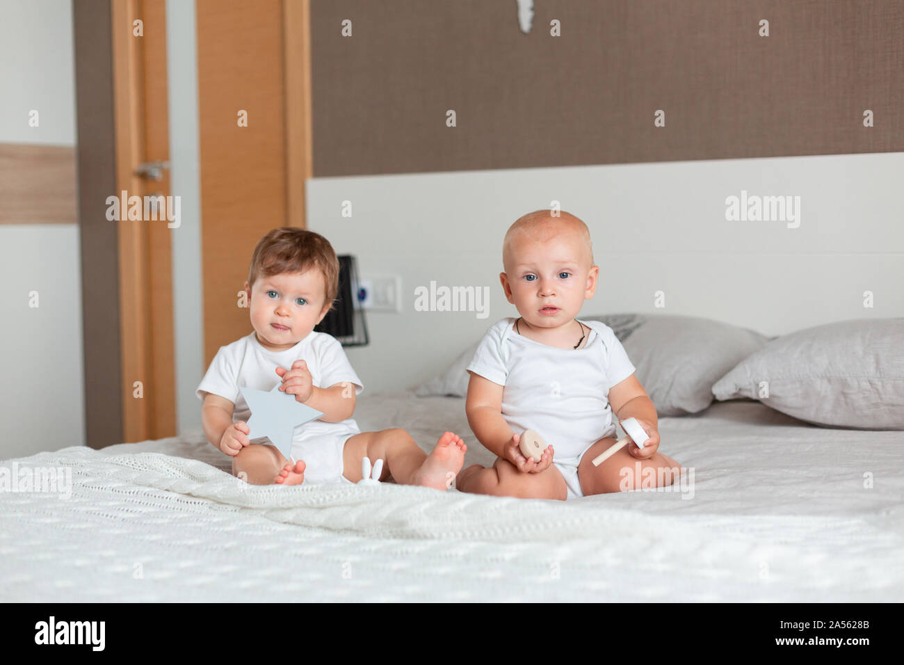 Two small happy babies sitting on a big bed in the bedroom Stock Photo ...