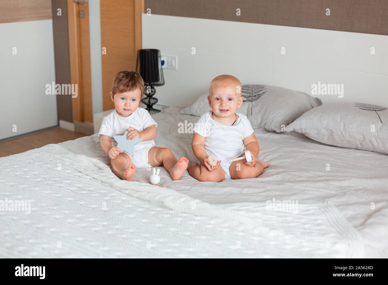Two small happy babies sitting on a big bed in the bedroom Stock Photo ...