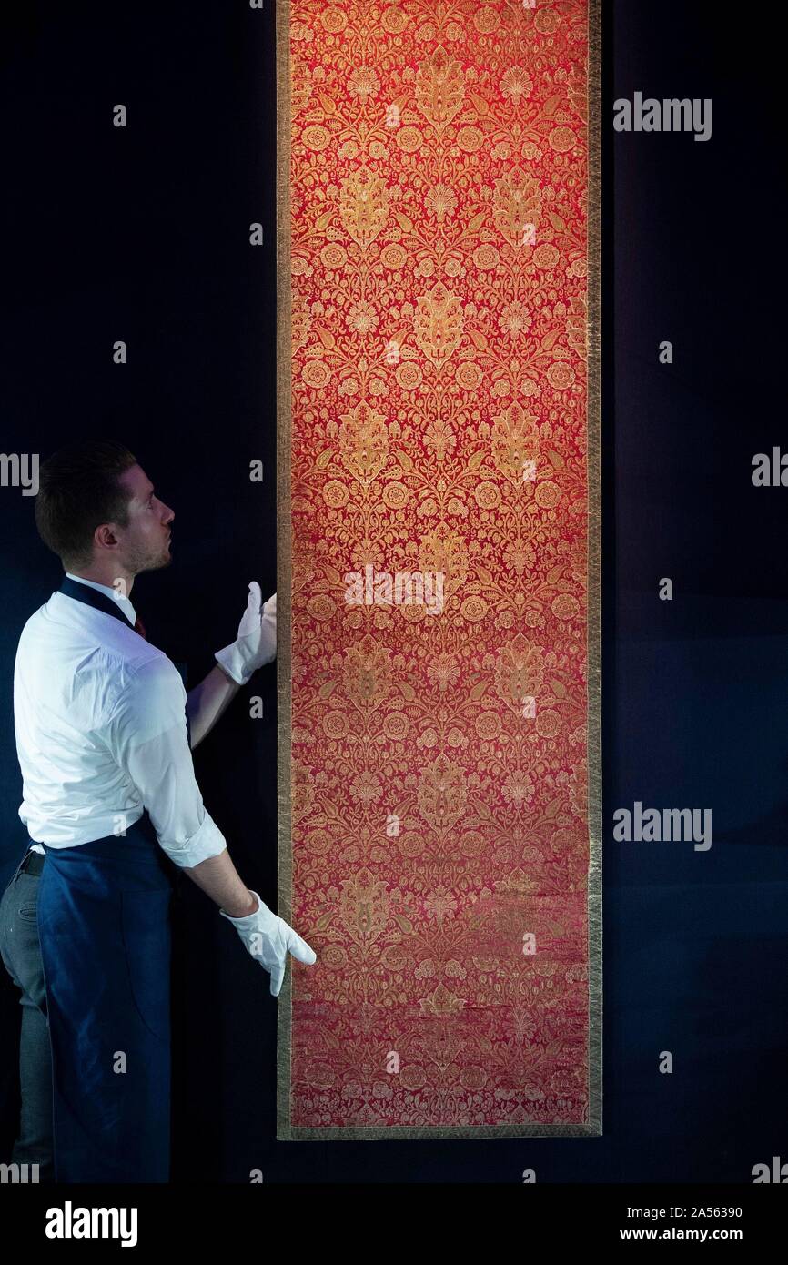 A staff member adjusts a rare Ottoman silk and metal-thread brocade panel, made in Turkey in the 17th century (est. £60,000-£80,000), during the preview of Middle Eastern Art Week at Sotheby's in London, ahead of their sale by auction on 22 and 23 October. PA Photo. Picture date: Friday October 18, 2019. Highlights of the sale will include a sumptuous leaf from the mythic 9th/10th century blue & gold Qu'ran, a dynamic painting of a great Indian epic wedding procession, jewellery including a talismanic Mughal emerald crystal weighing 363.9 carats, and paintings and sculpture by pioneering artis Stock Photo