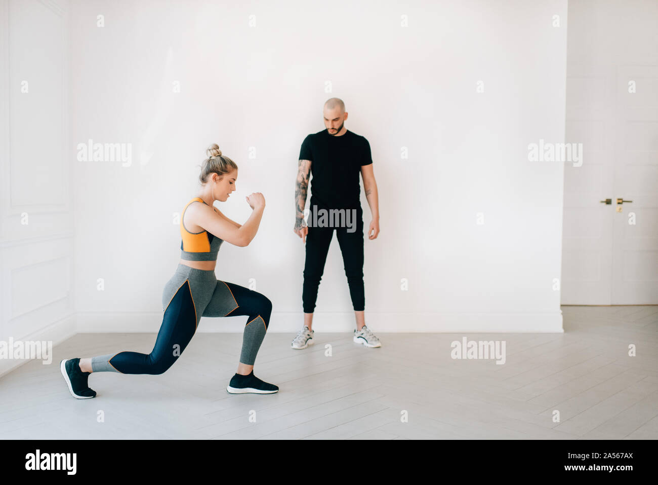 Fitness instructor observing woman doing lunges in studio Stock Photo