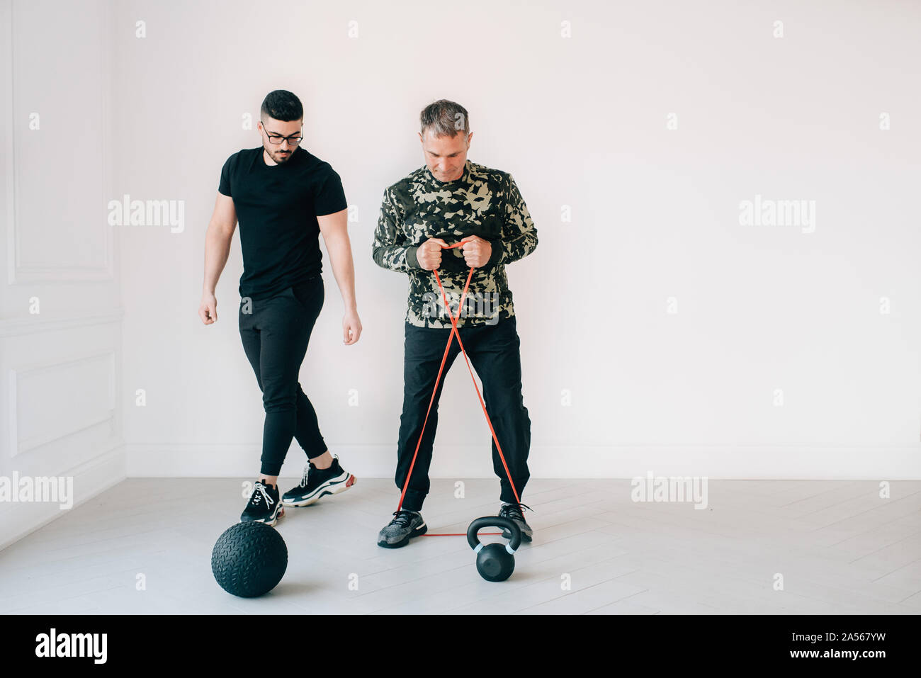 Fitness instructor observing man using resistance band in studio Stock ...
