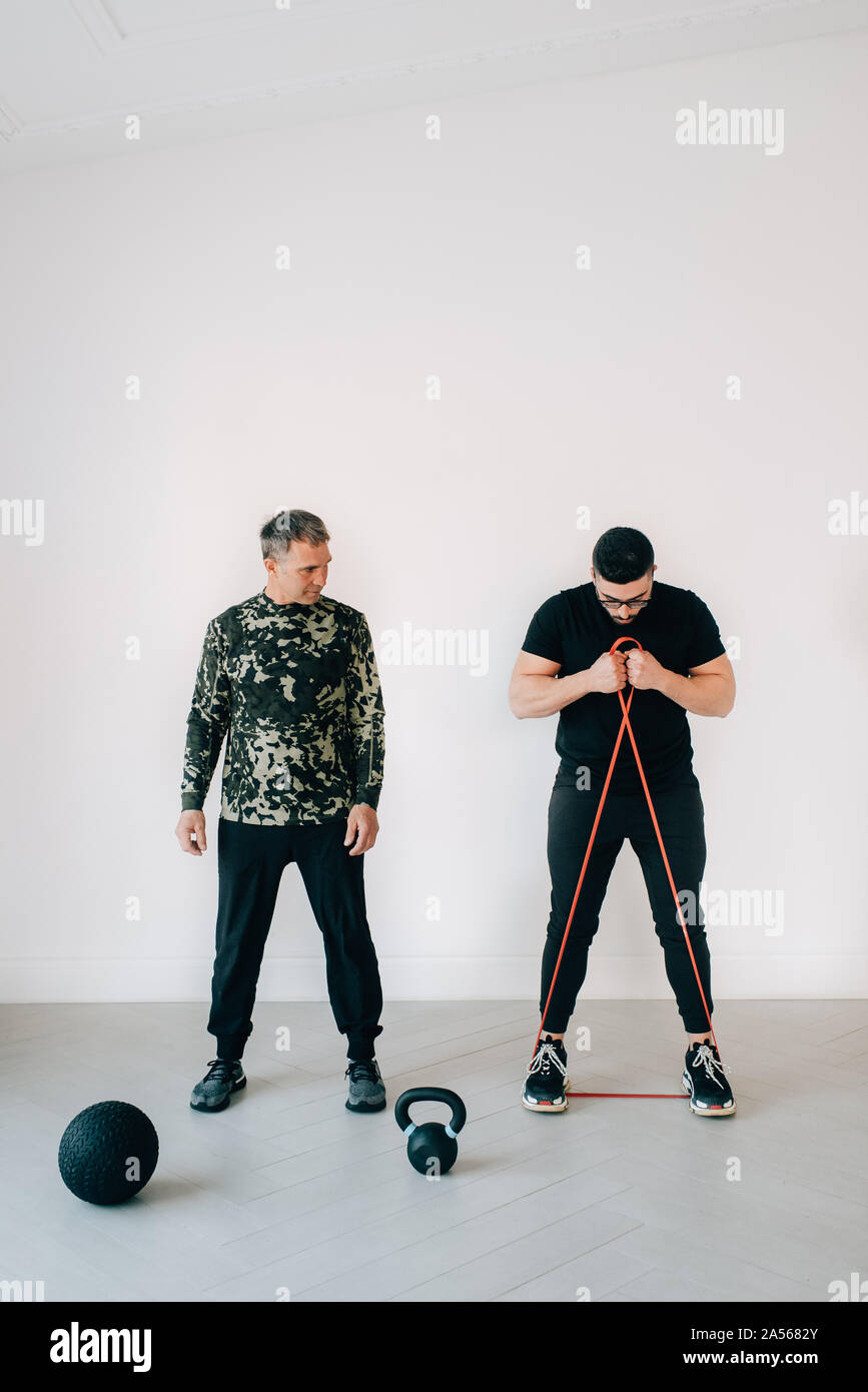 Fitness instructor teaching man using resistance band in studio Stock Photo