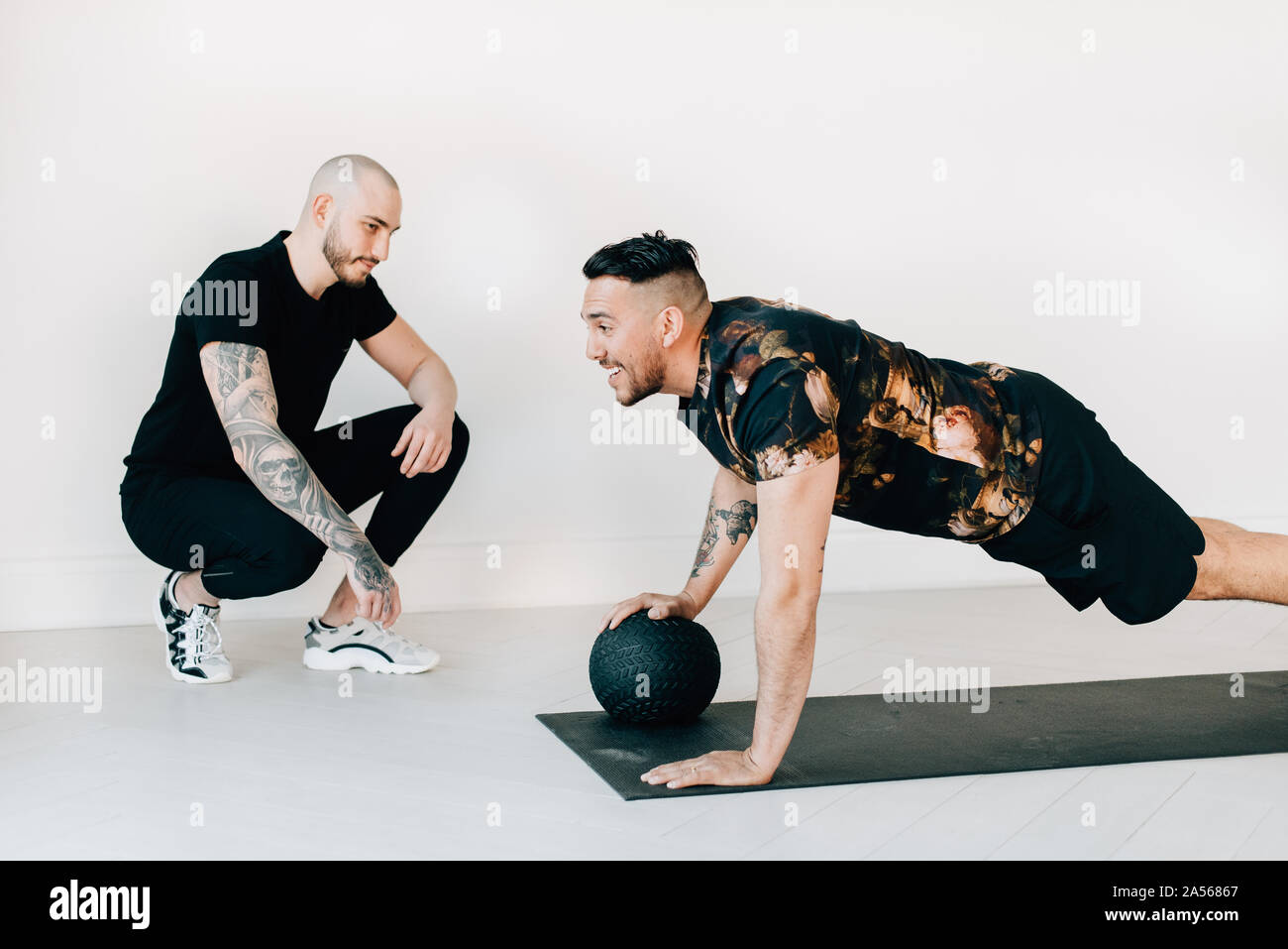 Fitness instructor observing man doing plank with medicine ball in studio Stock Photo