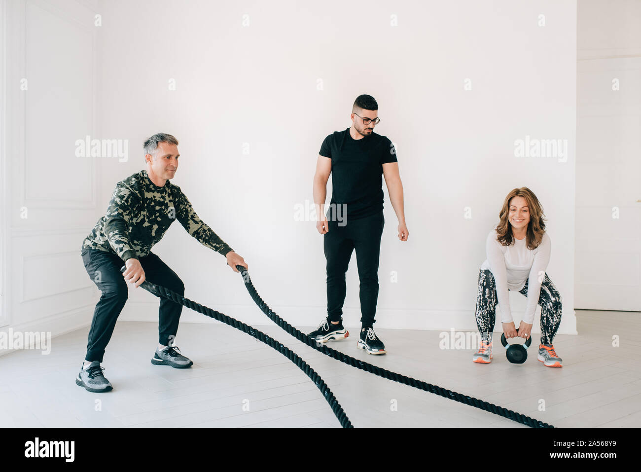Fitness instructor observing man using battle rope in studio Stock ...