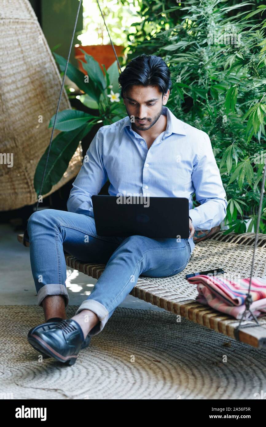 Businessman using laptop on swing Stock Photo