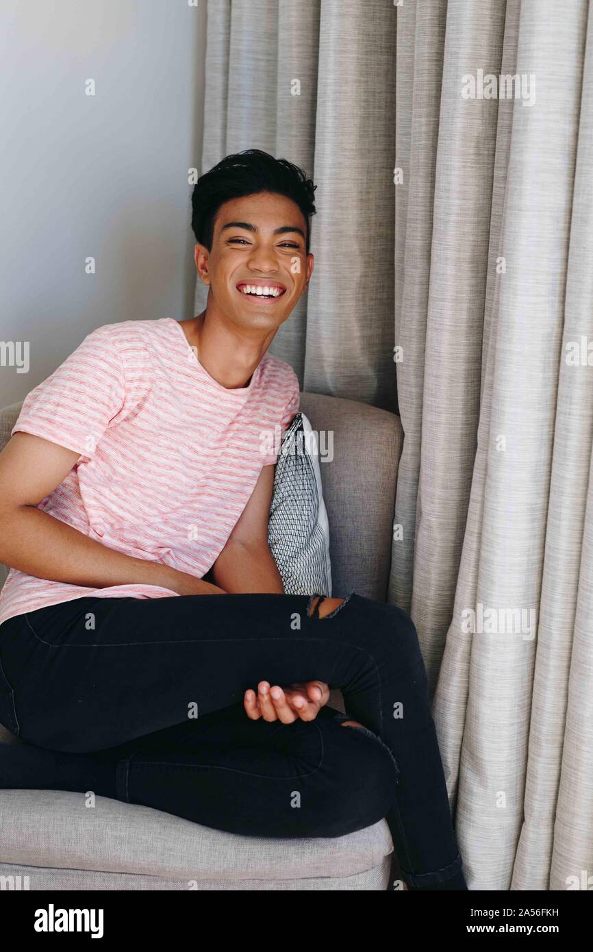 Young man sitting on bedroom chair laughing, portrait Stock Photo
