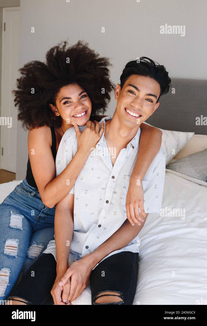 Happy young woman with arms around boyfriend while sitting on bed, portrait Stock Photo