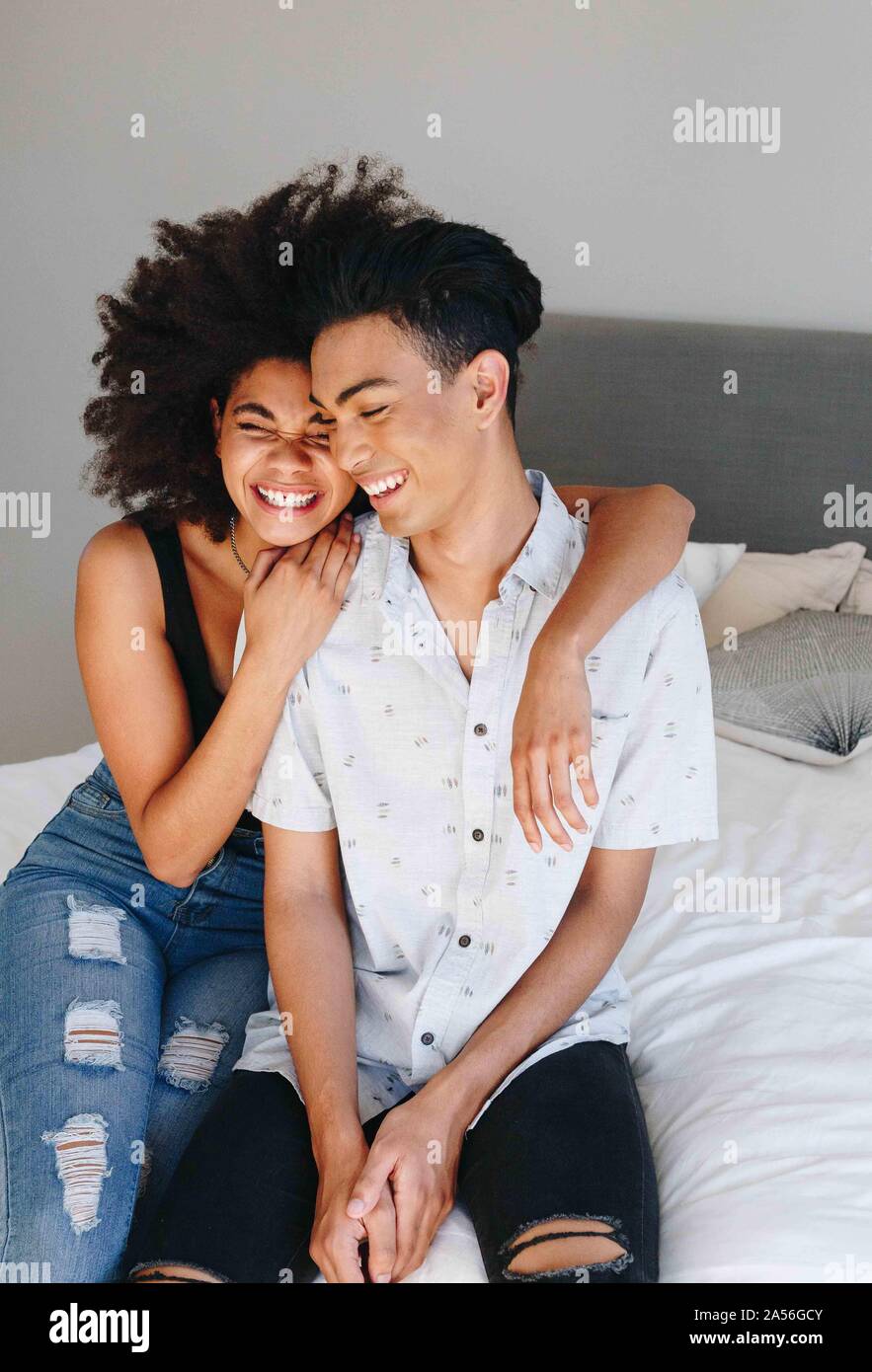 Happy young woman with arms around boyfriend while sitting on bed Stock Photo