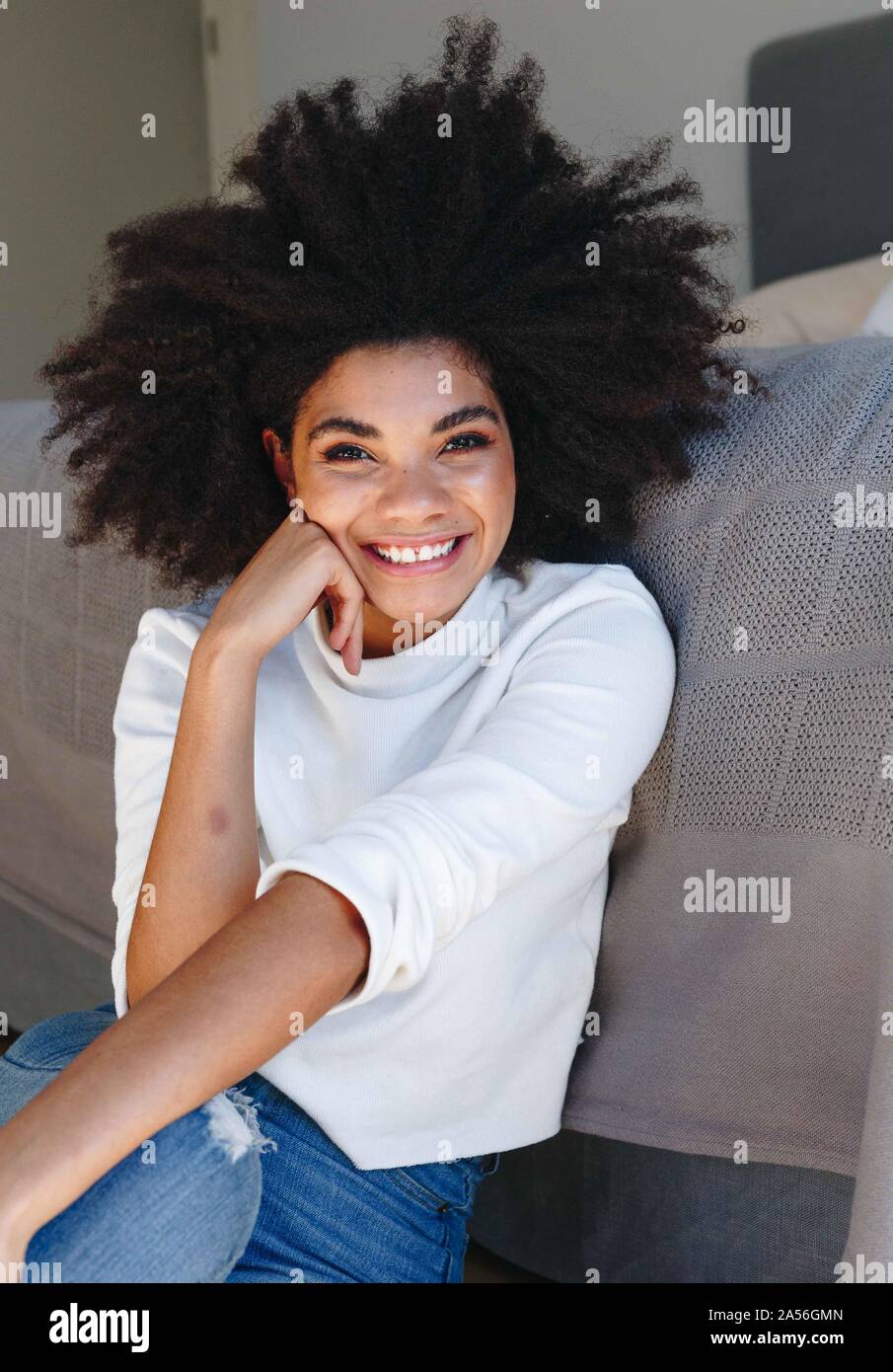 Happy young woman with afro hairstyle sitting on bedroom floor, portrait Stock Photo