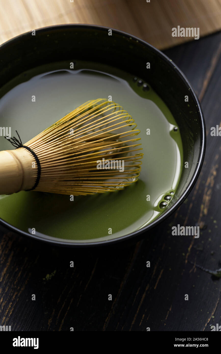 Still life of matcha tea preparation with whisk in bowl of matcha tea, close up, overhead view Stock Photo