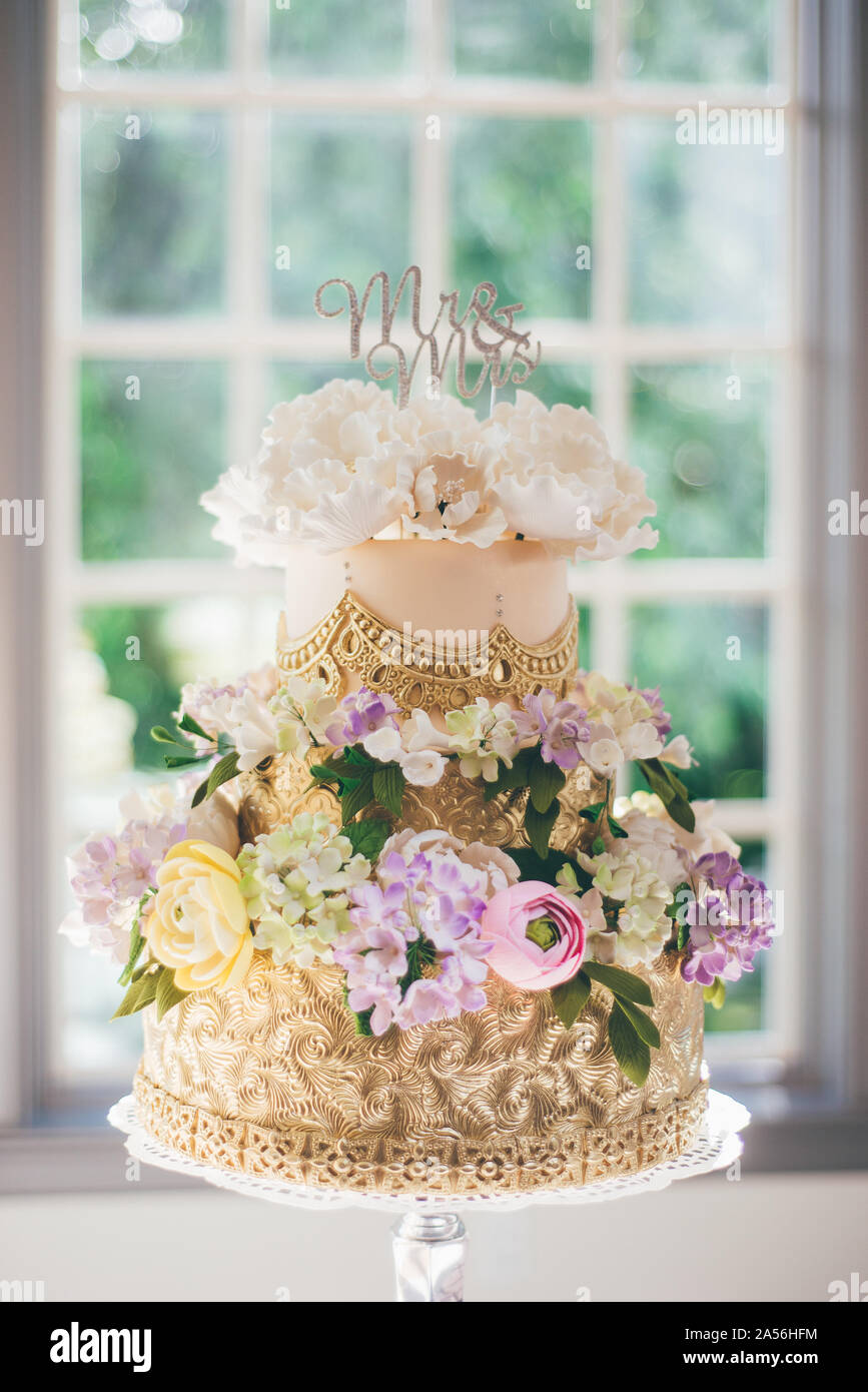 Mr and Mrs wedding cake decorated with gold patterns and icing flowers at wedding reception Stock Photo
