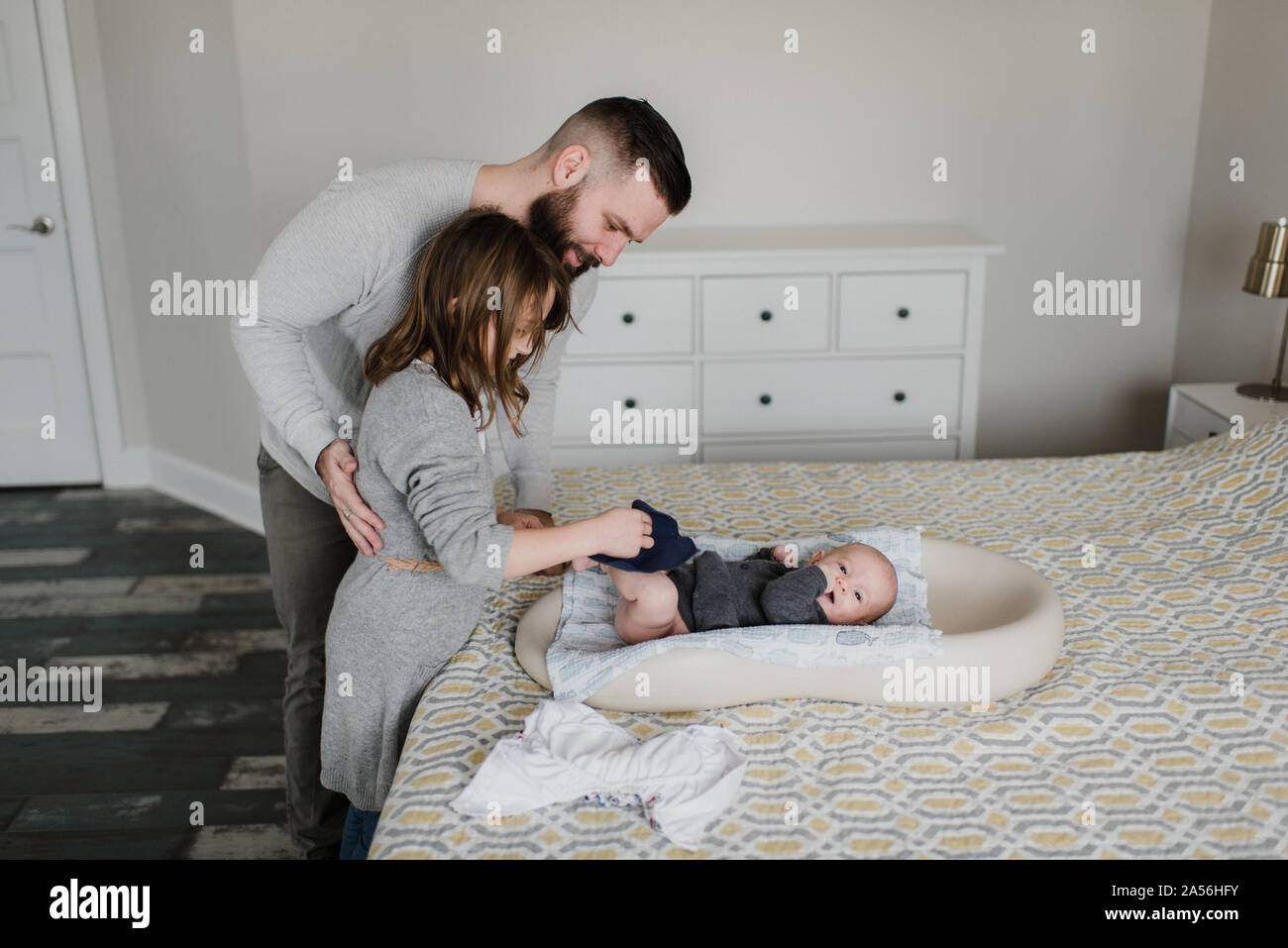 Girl with father changing baby brother's diaper on bed, side view Stock