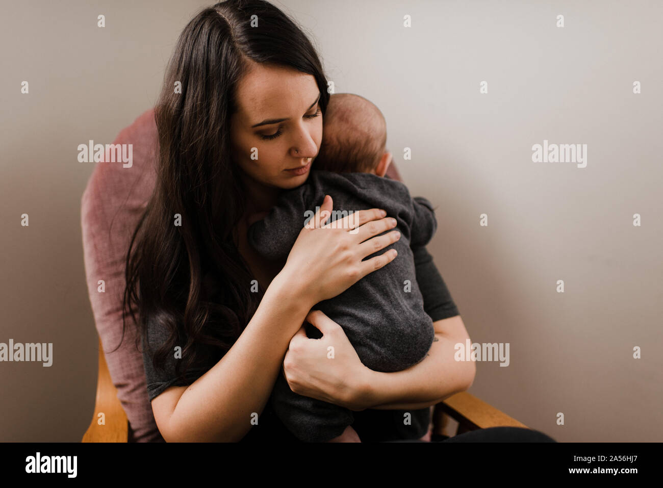 Young woman holding baby son in living room armchair Stock Photo