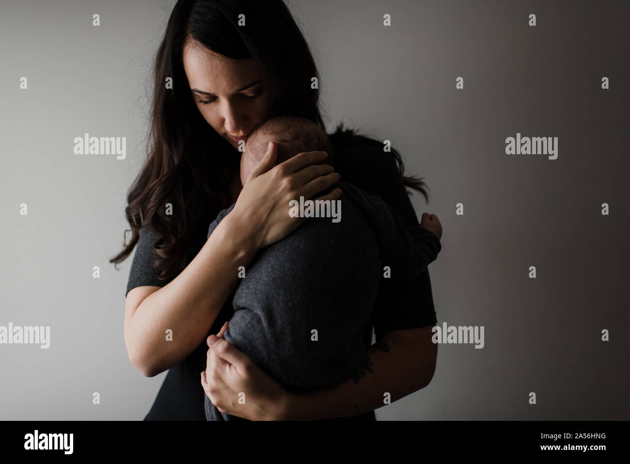 Young woman cradling baby son in arms, low key Stock Photo