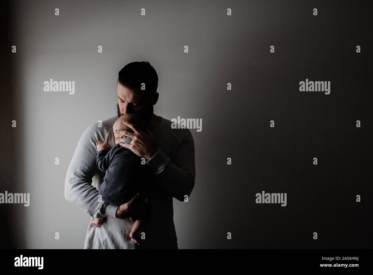 Young man carrying baby son in arms, low key Stock Photo