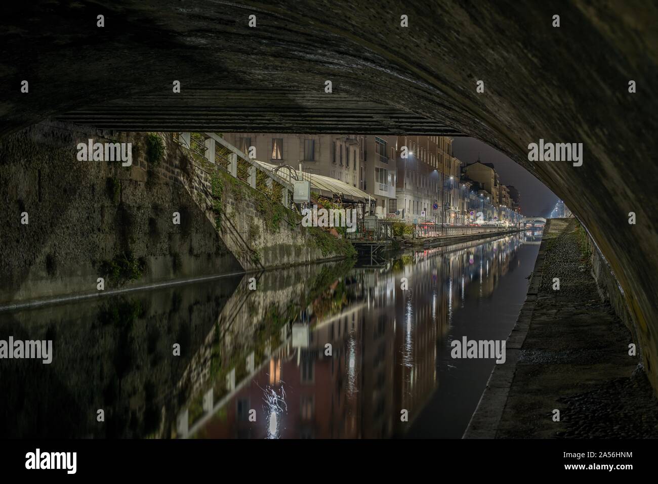 Horizontal shot of apartment buildings reflected in a lake under bridge at nighttime in Milan, Italy Stock Photo