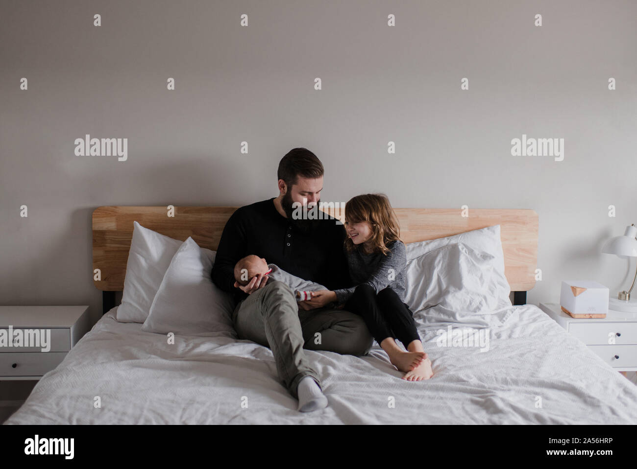Young man sitting on bed with baby son and daughter Stock Photo