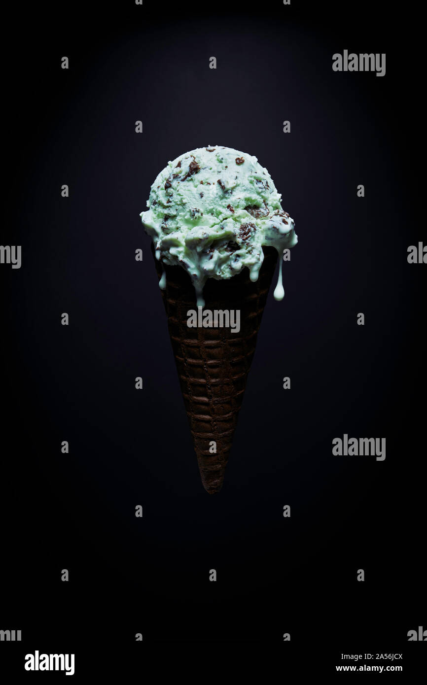 Chocolate chip mint ice-cream cone with melted droplets against black