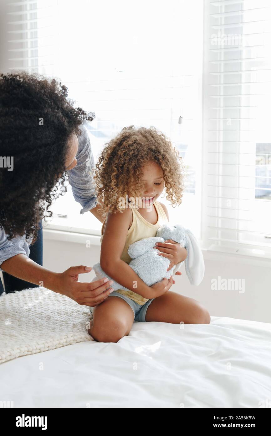 Woman talking to little girl cradling soft toy on bed Stock Photo