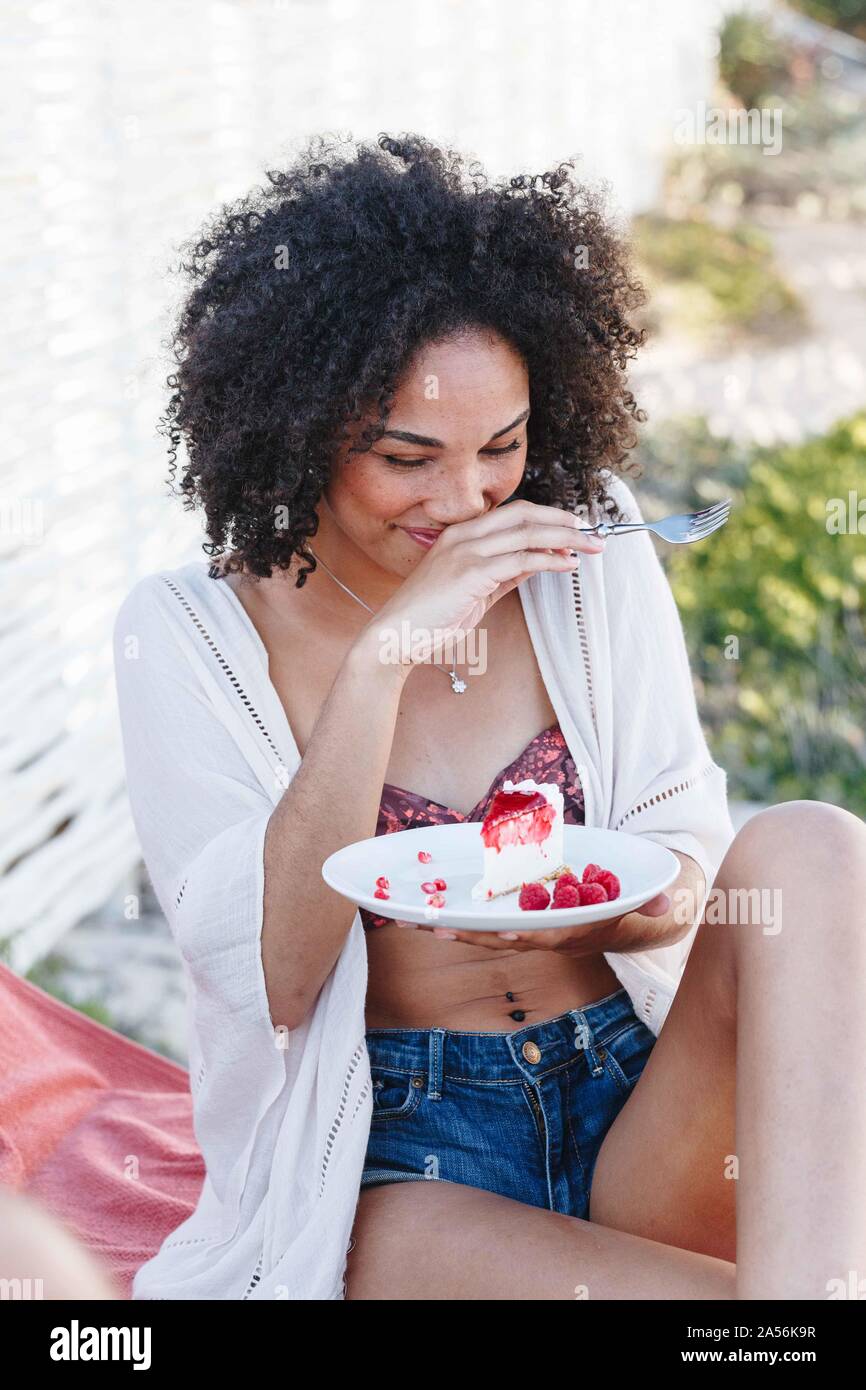 Woman holding plate of raspberry cake, covering mouth, giggling Stock Photo