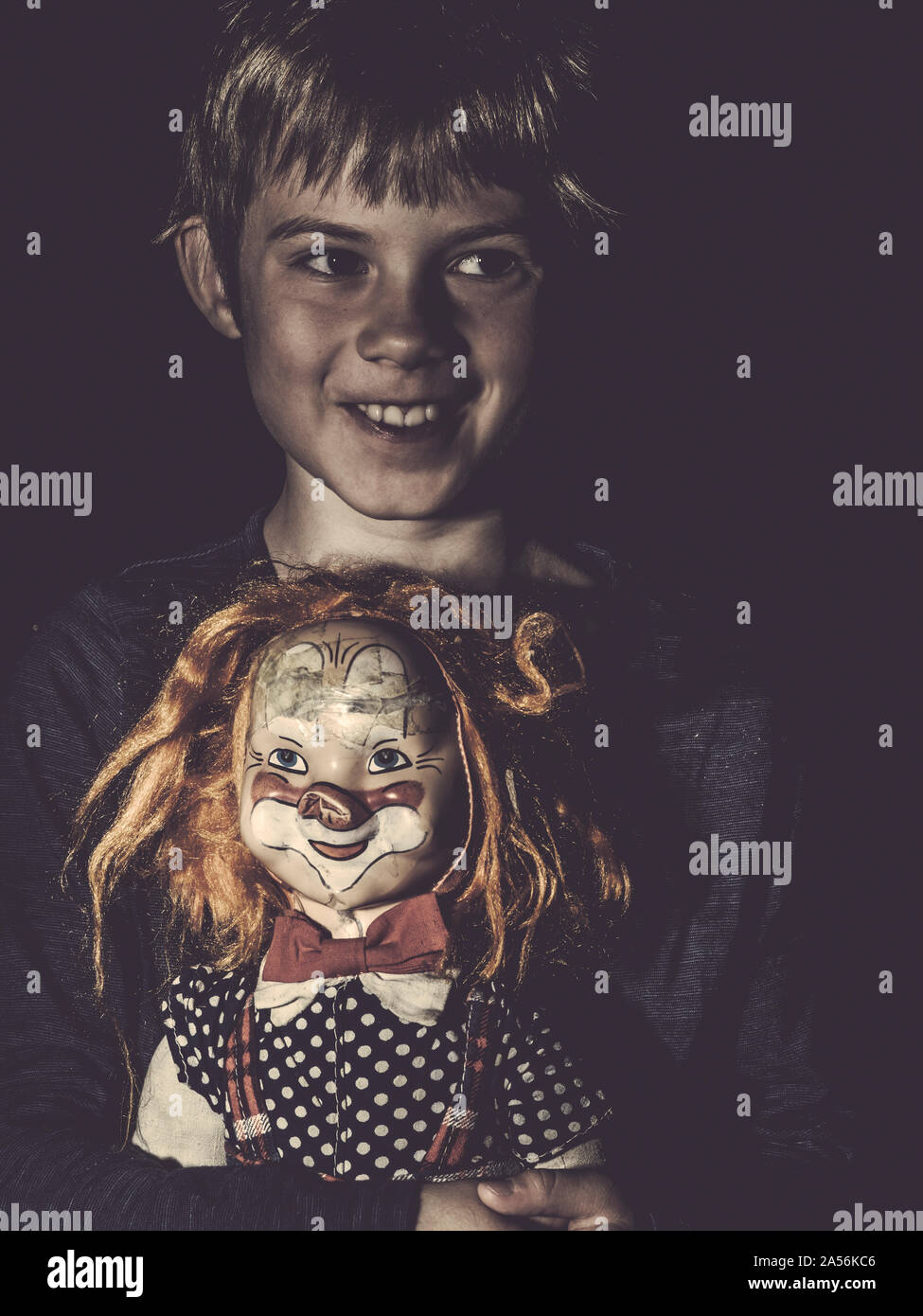 Photo of a creepy young boy holding an old doll for Halloween theme. Stock Photo