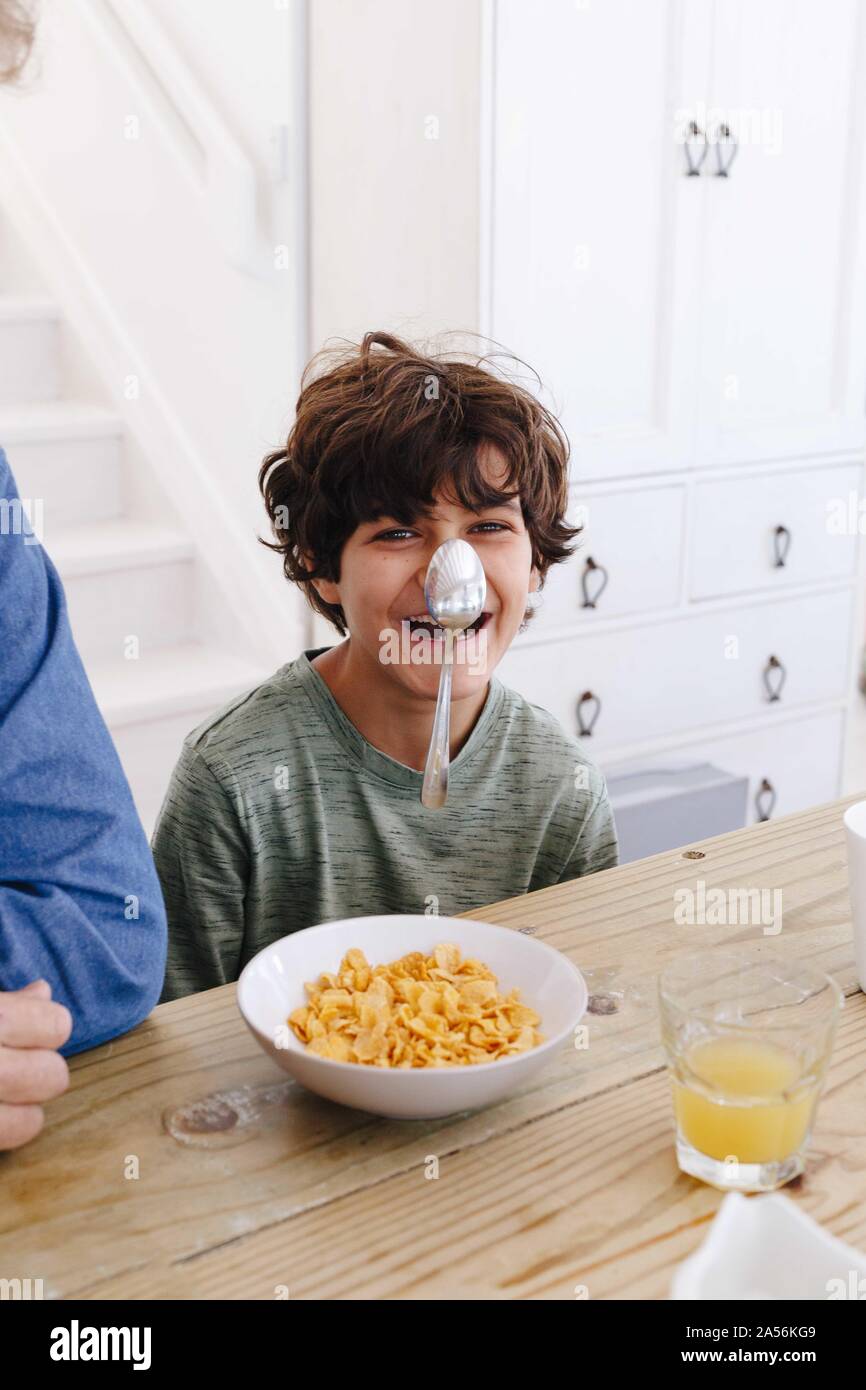 Boy laughing at spoon sticking on nose at breakfast Stock Photo