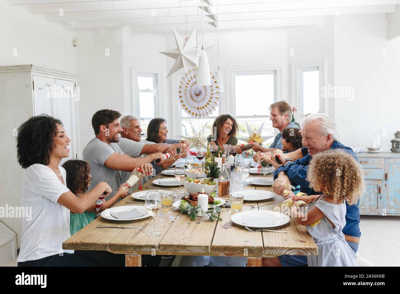 Family popping Christmas crackers together at dining table Stock Photo