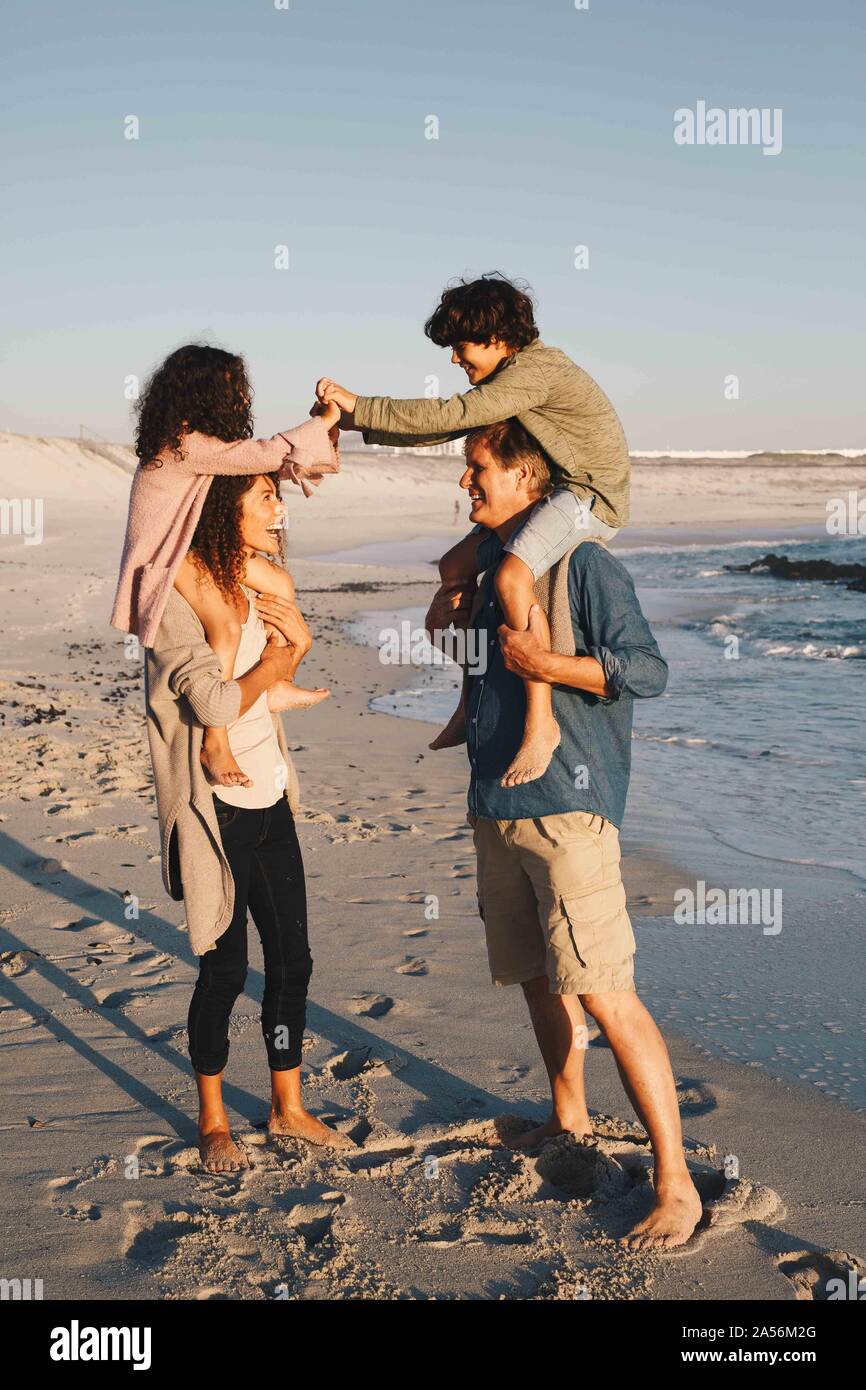 Children piggyback fighting on parents at beach Stock Photo