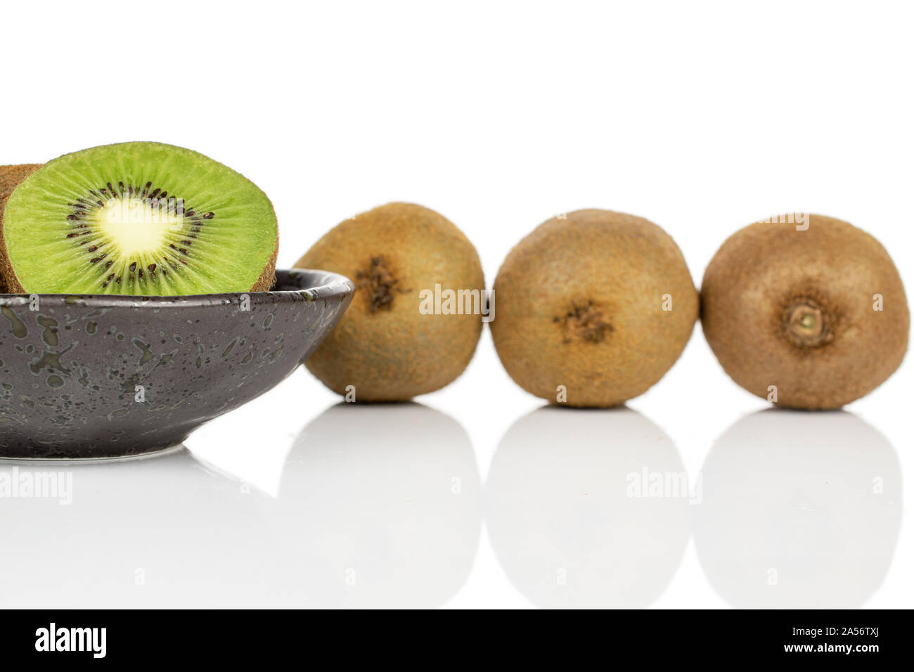 Group of three whole one half of exotic brown kiwi on glazed bowl isolated on white background Stock Photo