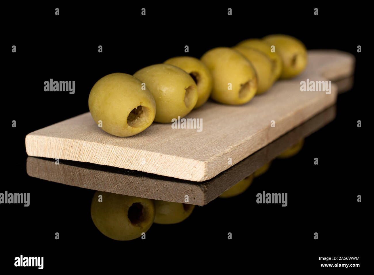 Group of seven whole marinated green olive on wooden cutting board isolated on black glass Stock Photo