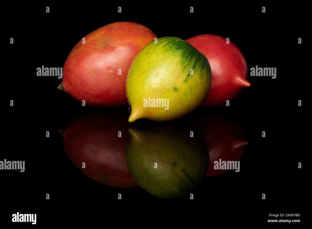 Group of three whole fresh tomato de barao isolated on black glass Stock Photo