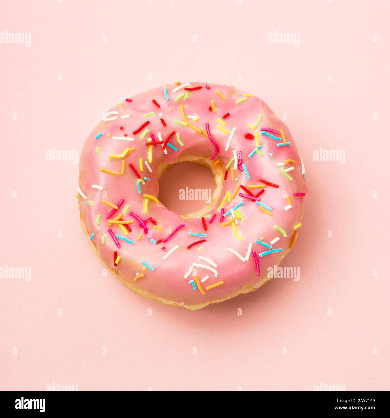 Pink donut decorated with sprinkles on coral background. Flat lay Stock Photo