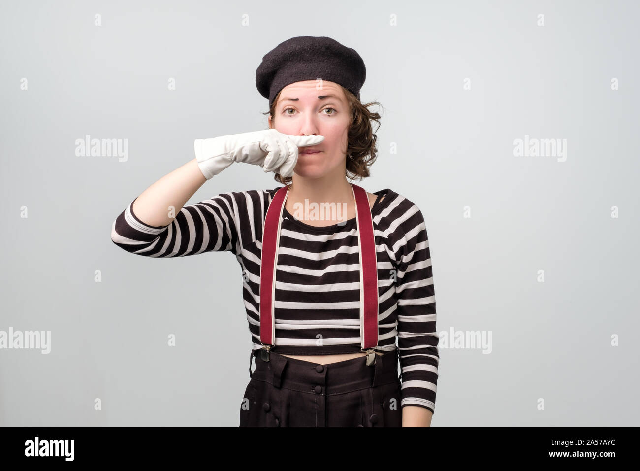 Young unhappy mime girl squeezing nose with fingers with disgust expression. Stock Photo