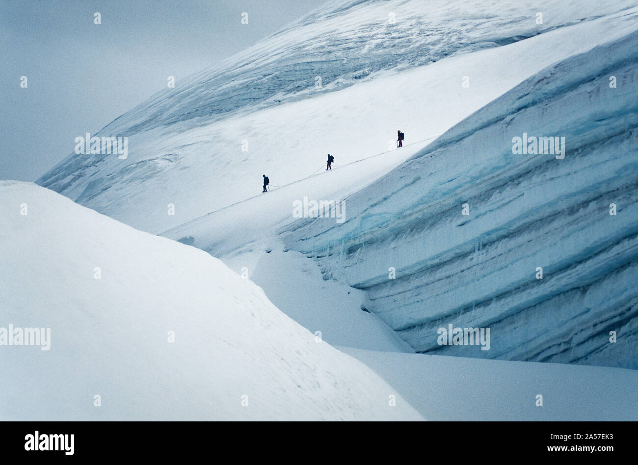 Figures of climbers pass a large crevasse high in the Swiss Alps Stock Photo